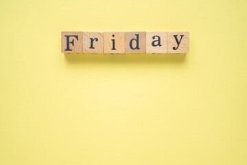 Text FRIDAY on wooden cubes with a copy space on a  yellow background. Flat lay view concept.