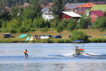 Old inboard motorboat with a tower towing the young wakeboarder on wake board on camp site and...