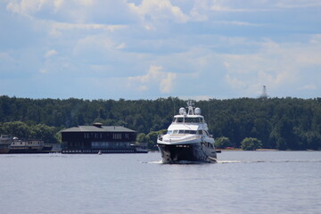 Beautiful river landscape with Luxury motor boat yacht slow floats on rcalm water on cloudy blue sky and green forest on coast background at summer day closeup front side view, vacation in Russia