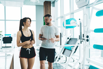 Athletic coach with woman near fitness machines
