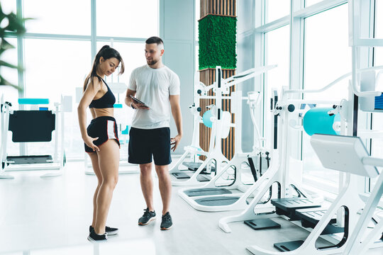 Slim woman consulting with instructor in gym