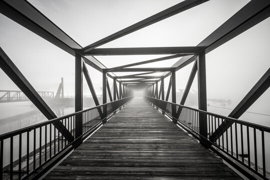 Fototapeta A grayscale shot of light at the end of a modern beautifully architectured bridge surrounded by fog