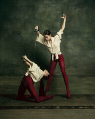Motion. Two young female ballet dancers like duelists with swords on dark green background....