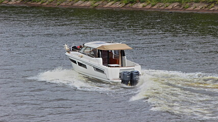 Fast floating cabin powerboat with two 200 hp outboqard motor on transom, back side view on calm water background at Sunny summer day, active recreation boating on river