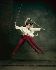 Fatal. Two young female ballet dancers like duelists with swords on dark green background. Caucasian models dancing together. Ballet and contemporary choreography concept. Creative art photo.