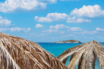 Umbrella made of palm leafs on Tigania beach in Sithonia, Greece with island on a background, sea and sky with clouds