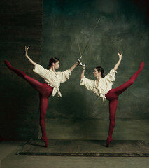 Flying. Two young female ballet dancers like duelists with swords on dark green background. Caucasian models dancing together. Ballet and contemporary choreography concept. Creative art photo.