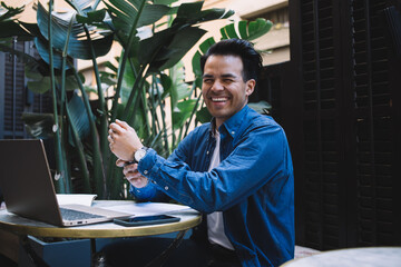 Happy self employed ethnic man at cafe table with laptop