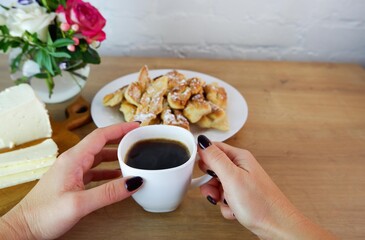 Cup of coffee in female hands, close-up. Homemade baked goods during quarantine. Homemade feta cheese on a wooden tabletop. Concept on the background of a white brick wall and a bouquet of roses.