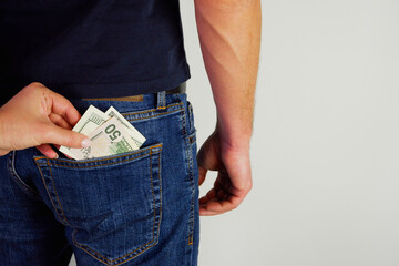 The woman pulls money out of the back pocket of the standing man's blue jeans. Close-up view of the hands. Place for your text.