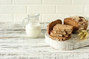 Sliced rye bread on wooden cutting board next to jug with milk. Tasty food close up. Homemade baked bread