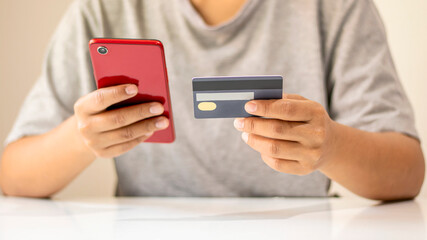 Asian man paying by credit card online while ordering on the internet at home, transaction idea using mobile banking application.