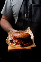 Masculine chef holding cheeseburger in a serving board