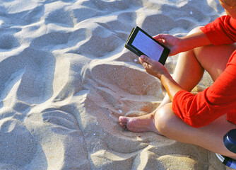 Woman reading ebook sitting on the beach