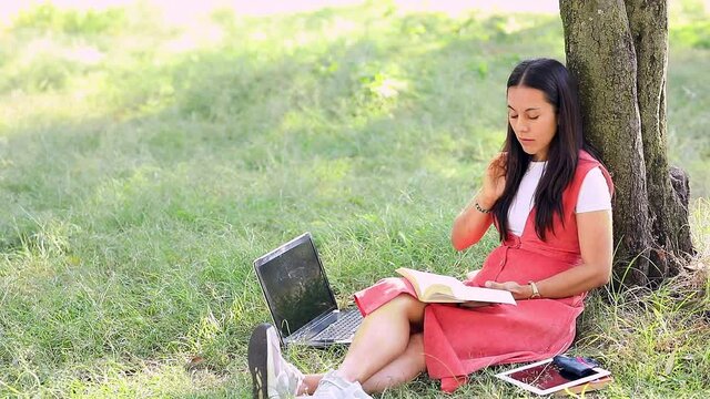 Mujer joven leyendo en el parque y  trabajando en su laptop. Concepto de chica latina trabajando en el parque