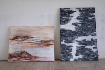 Modern art. View of two expressive paintings in the art studio. The paintings depict natural landscapes, a waterfall and the rocky sea shore at sunset.  