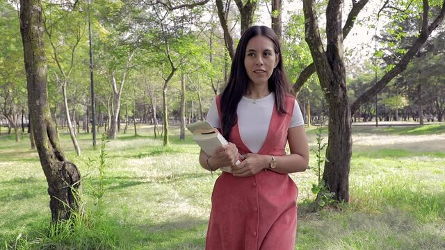 mujer latina caminando en el parque con libros en la mano.