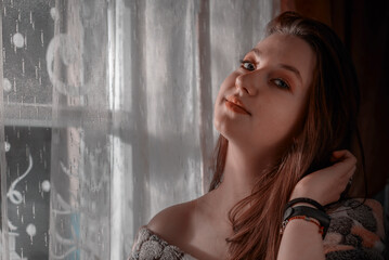 Fototapeta premium A cute girl is sitting by the window. The girl at the window