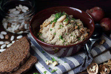 Kidney bean paste or appetizer with walnut and fried onion in a bowl on linen textile on dark black moody background, closeup, copy space, vegan and lenten food concept