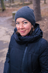 Beautiful smiling white teen girl in a winter black jacket and knit cap in the park