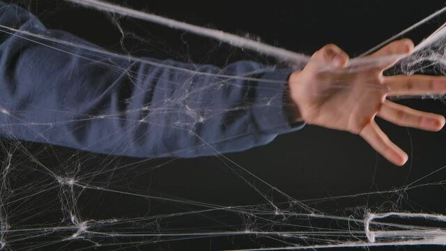 A man hand tears apart a terrible white web. Decorations for the celebration of Halloween night on a black studio background. Close up. Slow motion.