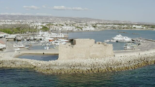 Drone flying over the old historic fort that stands on the shores of the Mediterranean Sea against the shoreline of which the waves crash. Aerial view Paphos Cyprus.