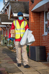 Hampshire, England, UK. 2020, Male courier delivering parcels and packages during Covid-19 epidemic wearing gloves and a mask.