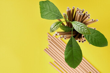 Drinking tubes made of paper and cornstarch, biodegradable material and eco paper glasses with green sprout leaves on yellow trend color 2021 background. Zero waste and plastic free concept. Top view.