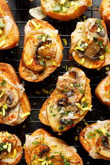 Mushroom and cheese  crostini sprinkled with spices and chopped fresh herbs top view. Delicious party food