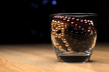 beads black brown golden in a glass on a dark background with a wooden table
