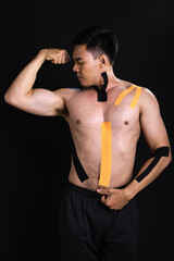Portrait of asian muscular man getting pain and putting kinesiology tape on his body