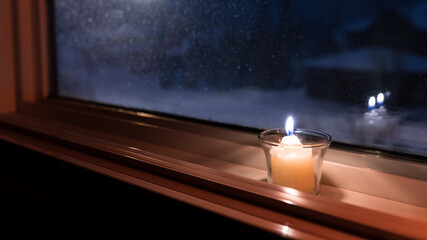Candle sitting on a window sill. Candle light glowing in the dark at night background. Christmas...