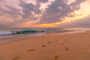 Beautiful ocean sandy beach under sunset sky with footprints in a sand.