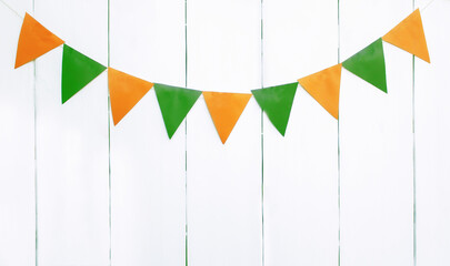 a garland of paper triangular flags of green and orange colors on a background of white wooden boards