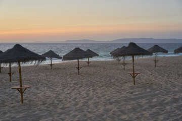 Empty beach at sunset in Comporta, Portugal with straw summer umbrellas