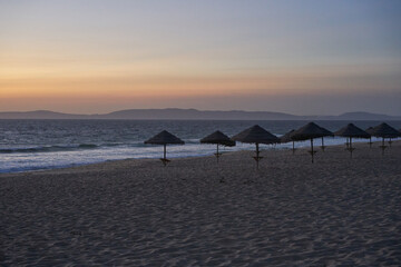 Empty beach at sunset in Comporta, Portugal with straw summer umbrellas