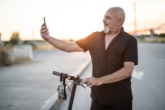 Attractive 60-year-old mature man on electric scooter posing at sunset for a selfie