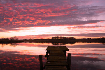Tranquil lake view with dramatic evening sky and red illuminated clouds.