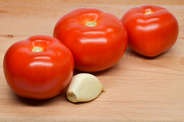Three red tomatoes on a cutting board with garlic in a row