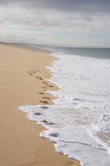 Wild empty beach with footsteps on the sand and ocean waves on the sand in Comporta, Portugal