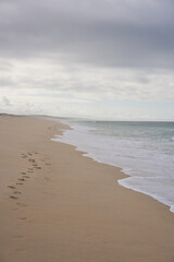 Wild empty beach with footsteps on the sand and ocean waves on the sand in Comporta, Portugal