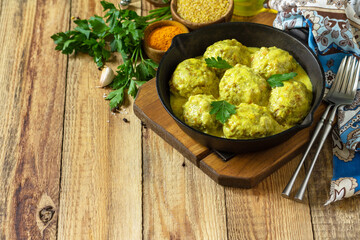 Meatballs with bulgur in sour cream and turmeric sauce in a cast-iron skillet on a rustic countertop. Copy space.