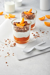 Healthy snack for two. Layers of apricot jam, poppy seed yoghurt and crunchy granola, decorated with fresh apricot wedges, served in plain glasses. Light positive airy photography