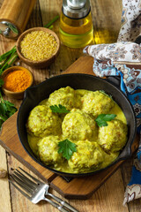 Meatballs with bulgur in sour cream and turmeric sauce in a cast-iron skillet on a rustic countertop.