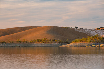 Desert like hill landscape with reflection on the water on a dam lake reservoir at sunset in Terena, Portugal