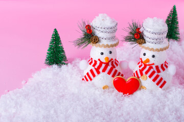   Happy Male and Female Snowmen and minimal Winter landscape on light pink background.