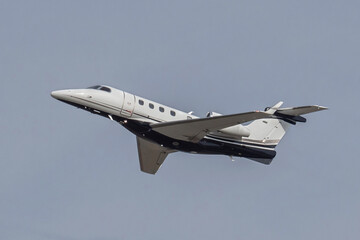 White small turbofan-powered business jet airplane flying in the air after takeoff from airport. Fast modern aircraft for air transportation. Aviation technology. Travel and business concept.