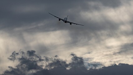 Unique dramatic dark gray clouds on dynamic cloudy sky background. The silhouette of airplane rising upward after takeoff. Storm weather conditions. Fast transportation, modern transport technology.