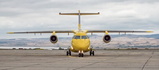 Front view of yellow airplane. Jet aircraft taxiing on airport apron, dynamic dark grey cloudy sky background. Modern technology in fast transportation, private business travel, charter flight.