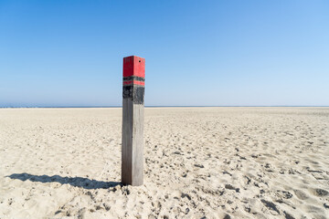 Close up of a single red beach pole or column on an empty beach at the Dutch North Sea in summer with blue sky - Powered by Adobe